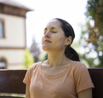 Person sitzt mit geschlossenen Augen auf einer Bank.
